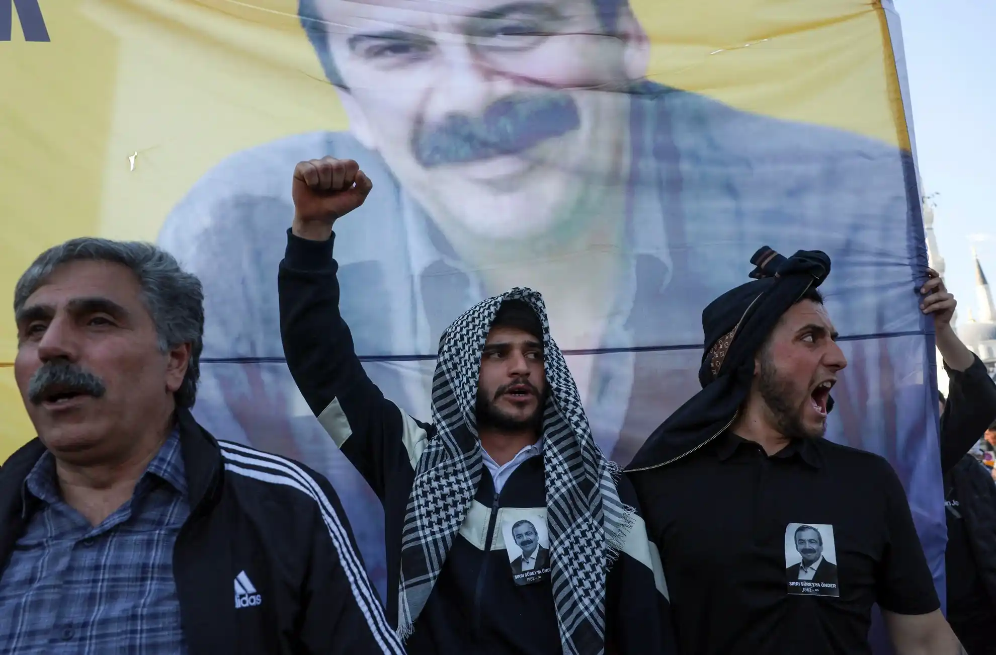 Люди выкрикивают лозунги перед портретом Сирри Сурейи Ондера