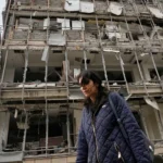 Женщина проходит мимо поврежденной больницы